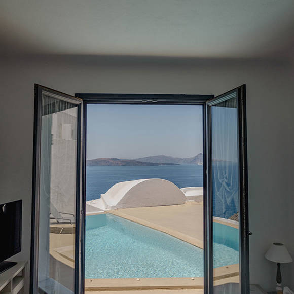 Grand Ambassador Santorini Petit Suite suite view through open doors to private pool terrace and caldera